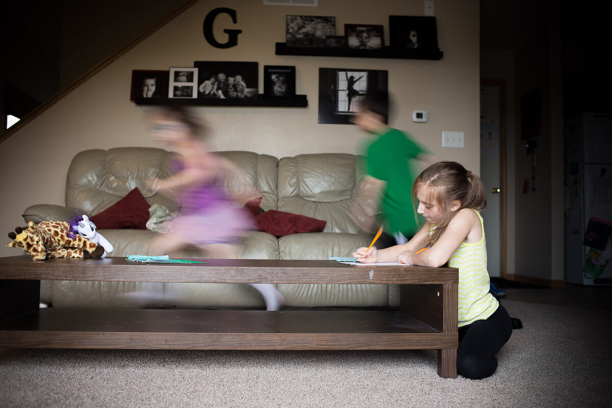 siblings run circles around coffee table while oldest finishes homework