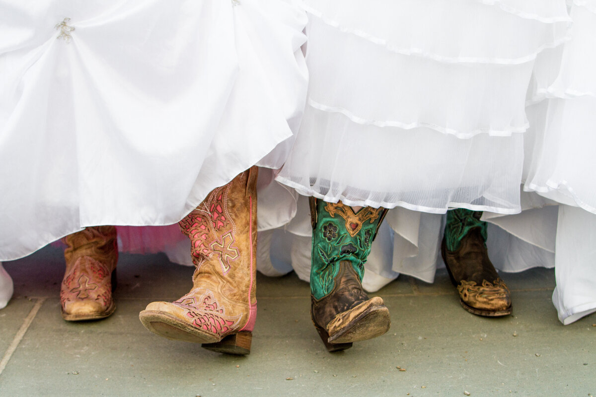 Close up view of cowboy boots under wedding dresses.