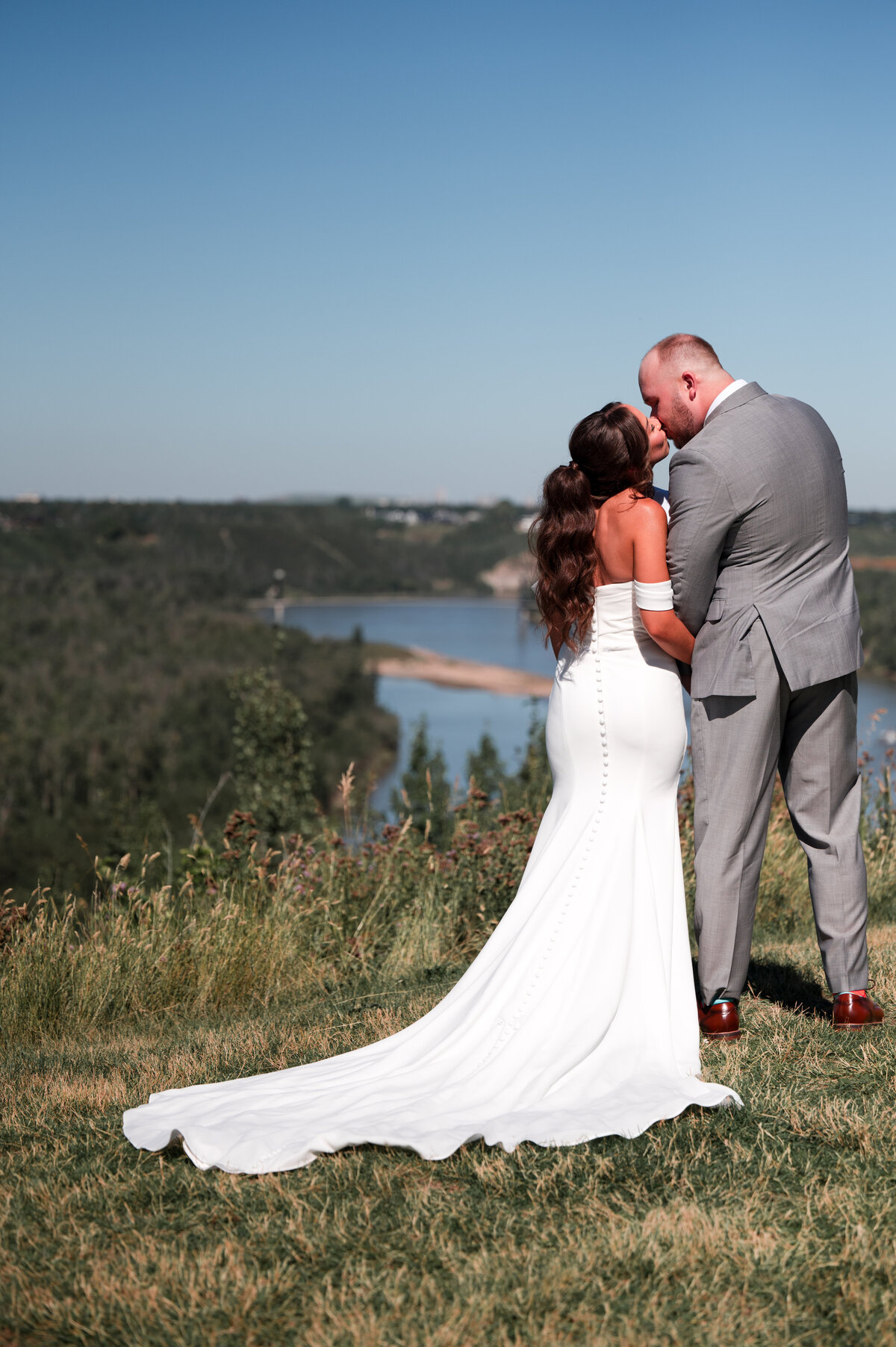 bride and groom stand on a hill facing the Edmonton river valley