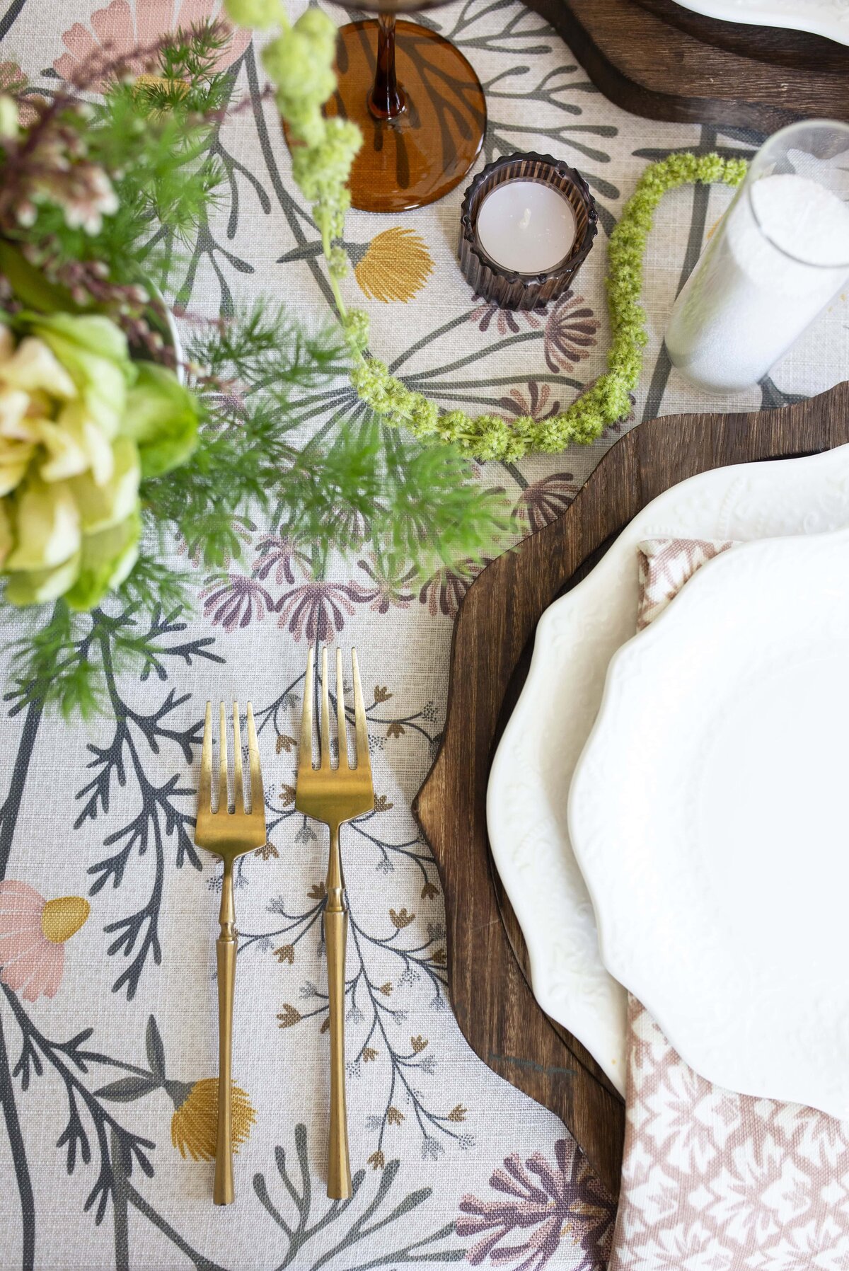 table settings at a spring wedding. Irregular shape white plates on a wooden charger, gold silverware and floral pattern linens by curated events raleigh.