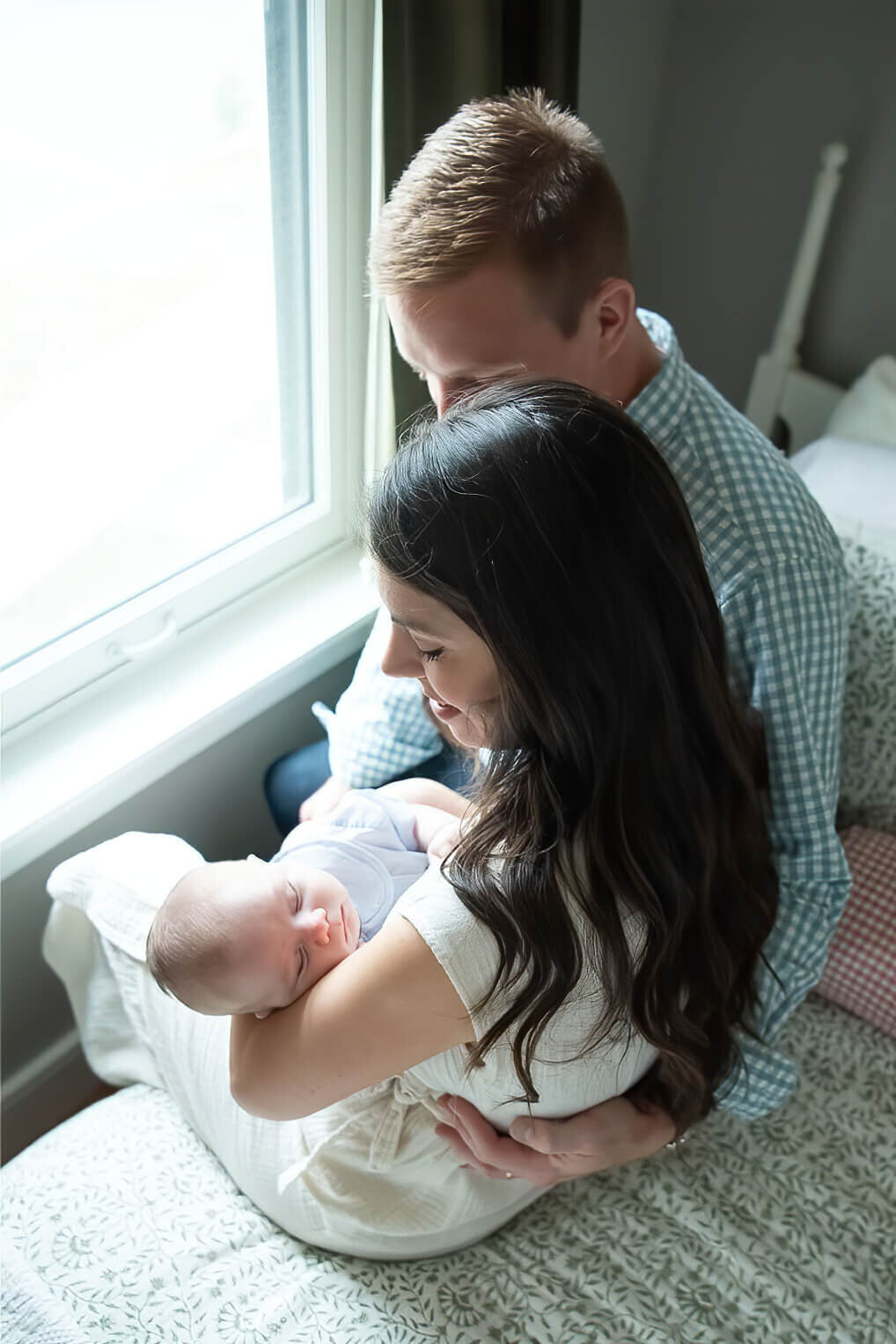 Two parents sit by the window of their Salem home and look down at their sleeping newborn.