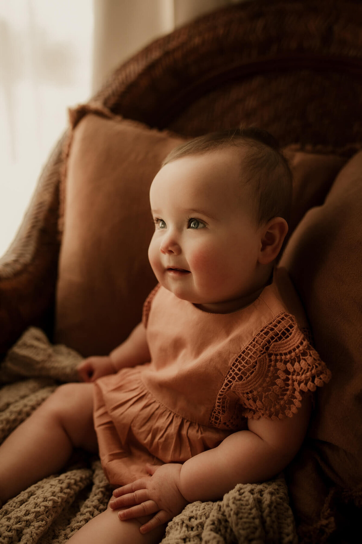Baby girl in a rose colored romper sitting in a chair for a studio portrait session in Oklahoma City.