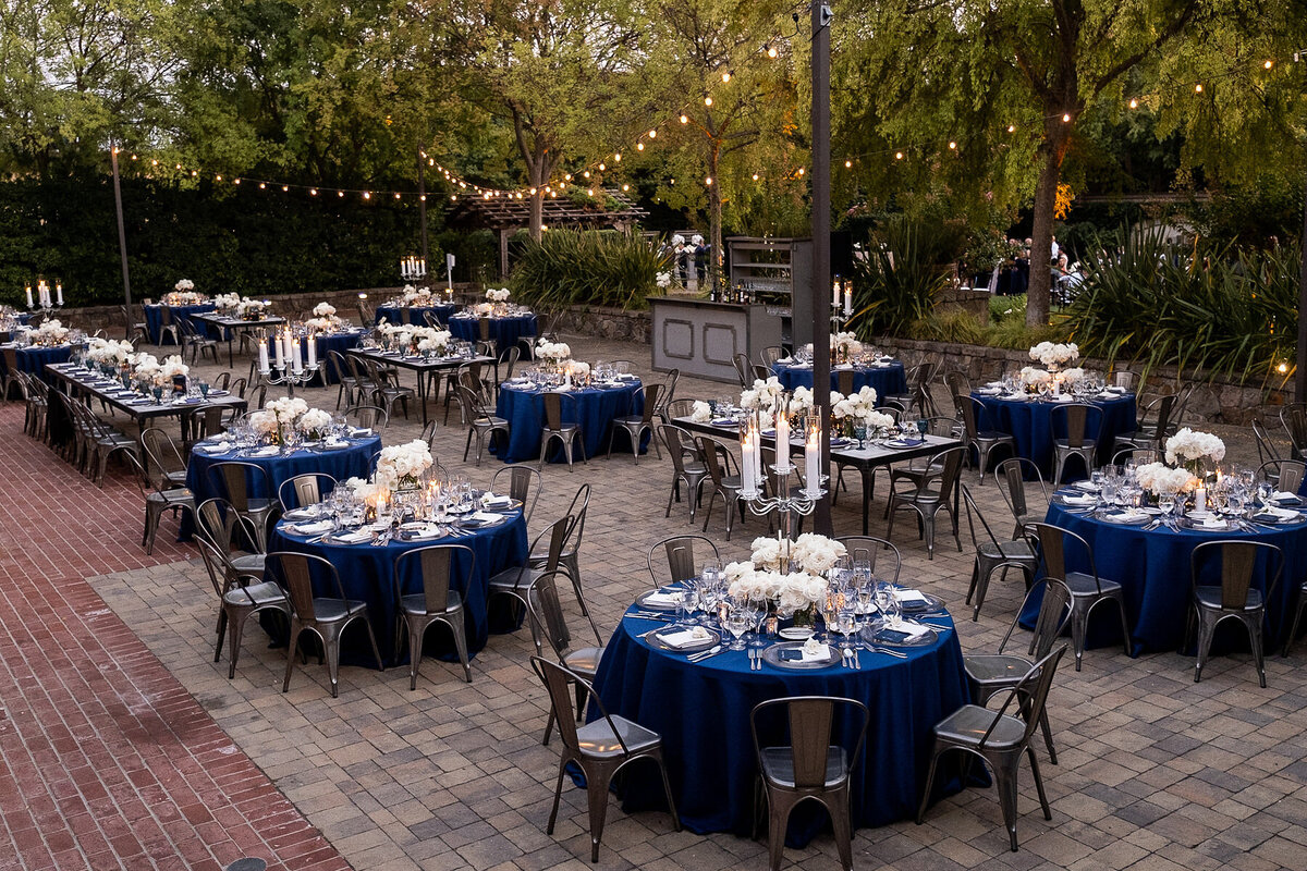 San Francisco Bay Area wedding photographer captures elegant evening reception setup with navy linens and string lighting on stone patio at Estate Yountville in Napa Valley