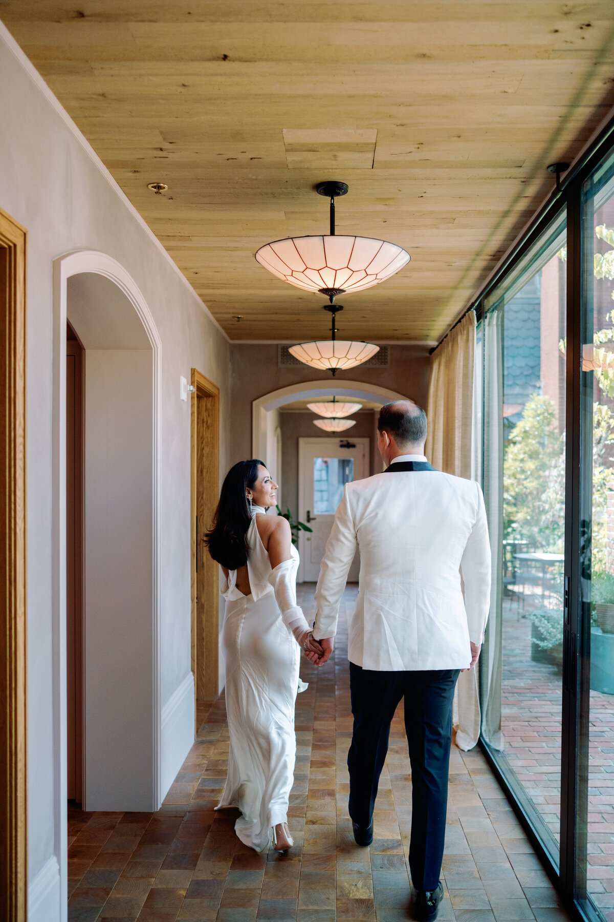Groom adjusts his jacket while standing with the bride in front of a glowing chandelier before their ceremony.
