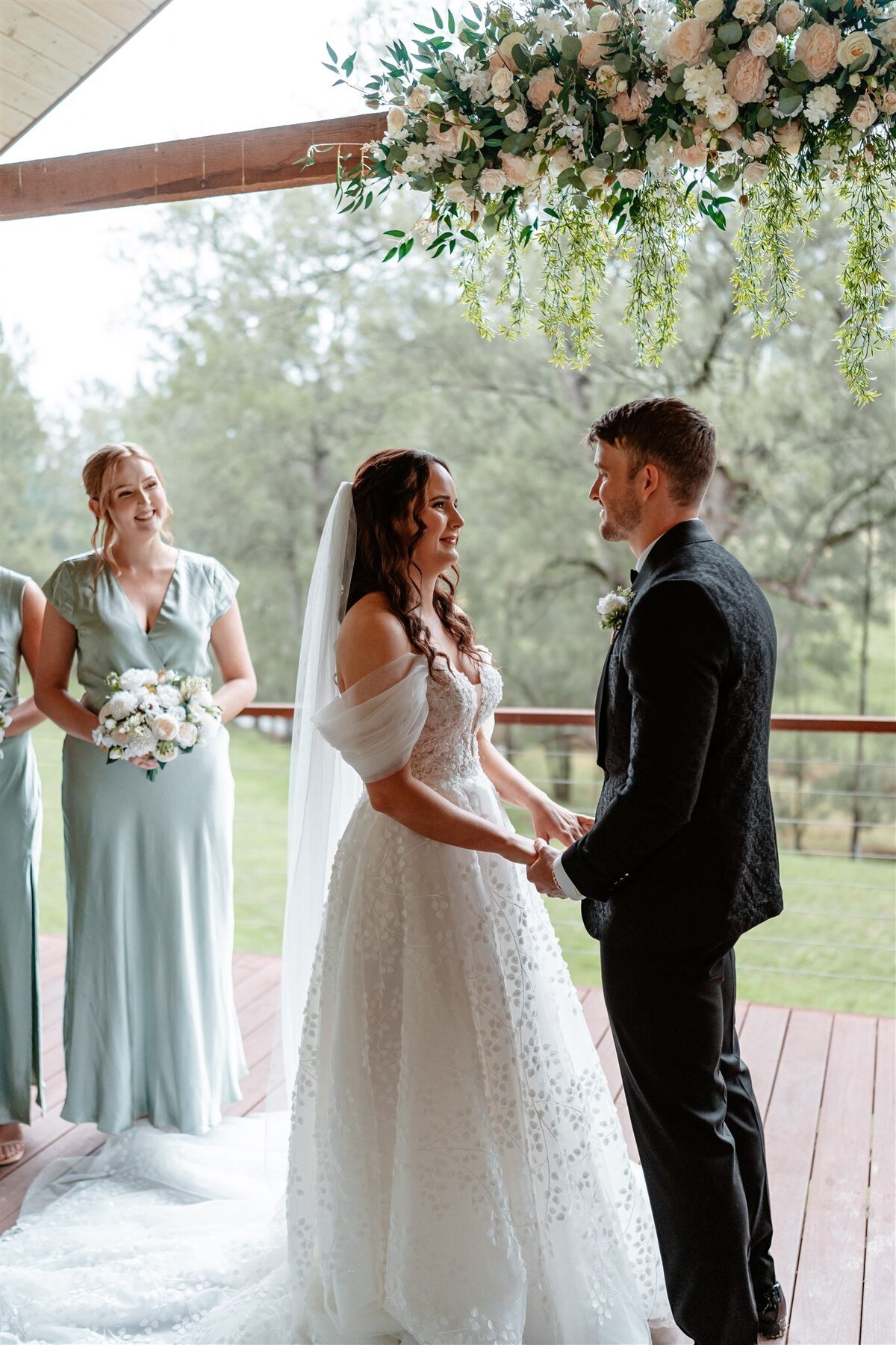 A radiant bride, clutching a bouquet of ivory roses, exchanges heartfelt vows with her groom under a cascading arch of fragrant blooms.