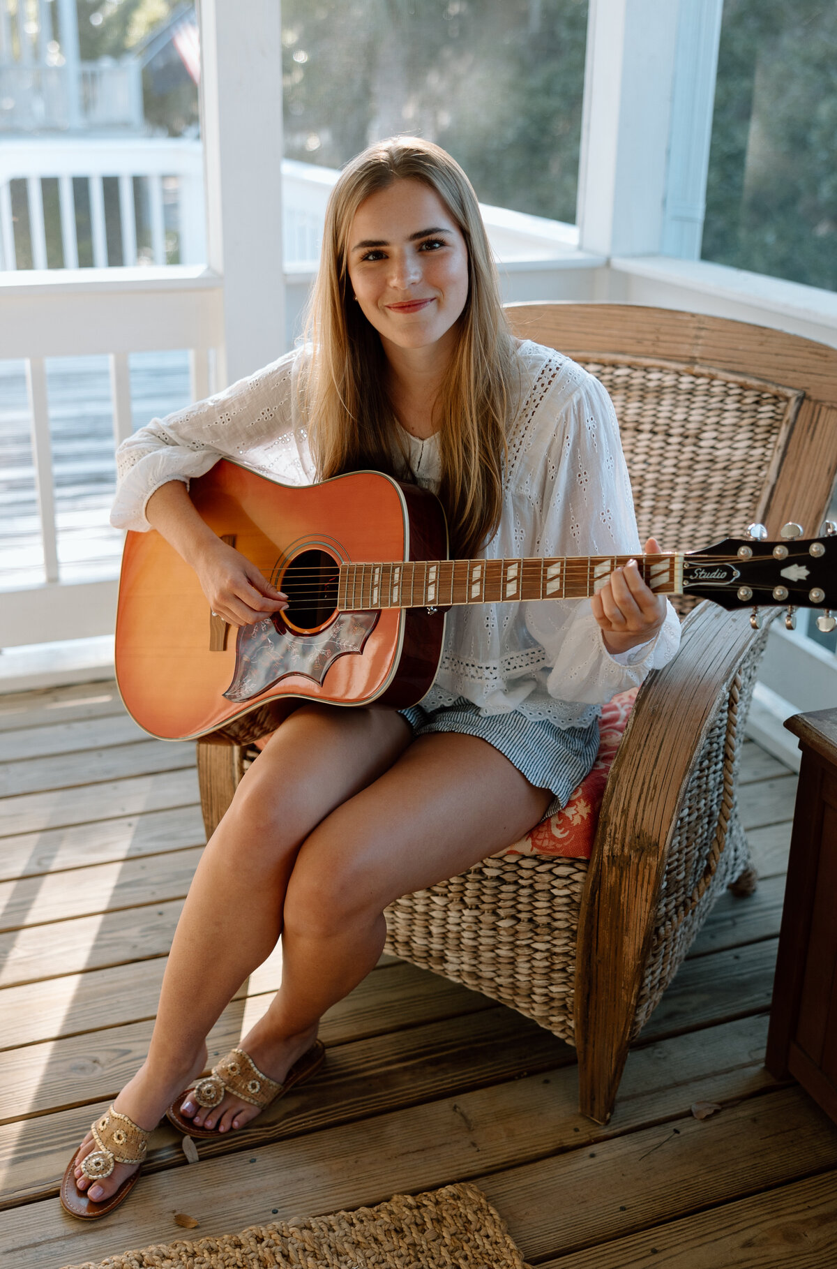 Senior photos at Edisto beach, senior sits on porch with a guitar