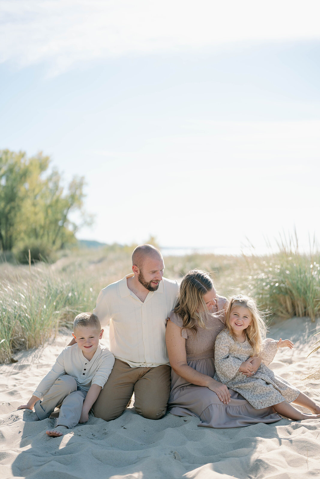 The Loza family sitting together in the warm sand at Weko Beach during their mini photo session in Bridgman Michigan.