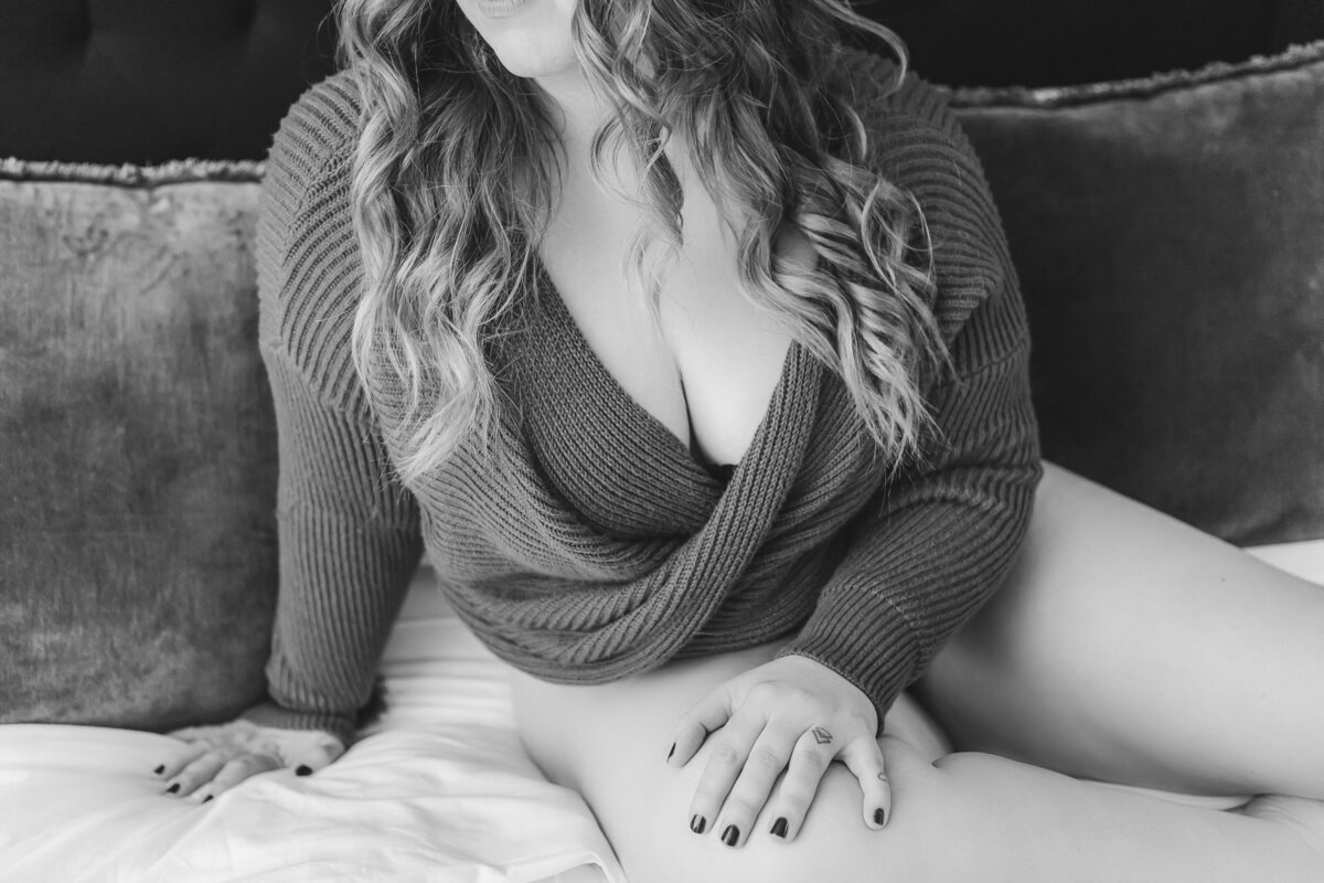 A woman sitting on a bed wearing a red sweater, softly smiling while showing off her relaxed pose.