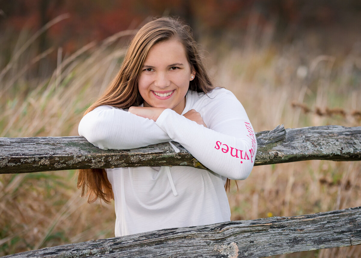 Fall senior girl by a fence at a farm