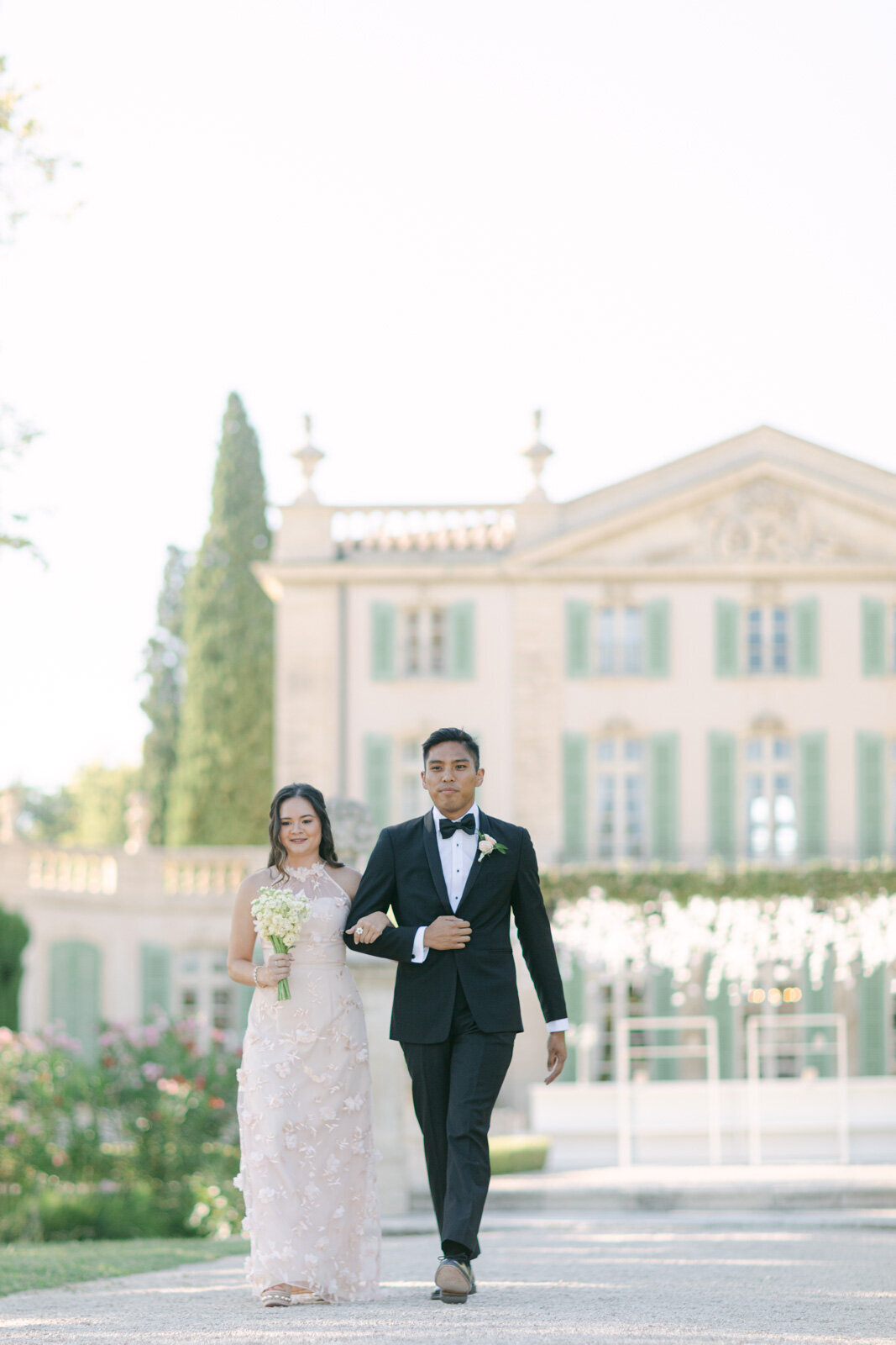 Bridesmaid and groomsman walking together at luxury Provence wedding in front of château.