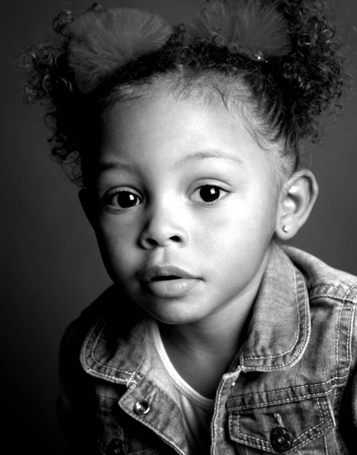 A black and white photo of a young girl smiling, with soft lighting highlighting her features.