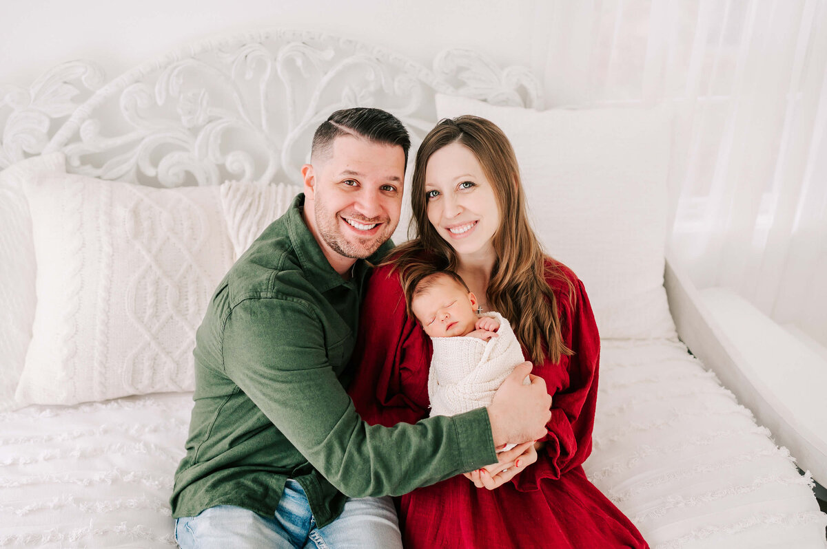 Branson MO newborn photographer Jessica Kennedy of The Xo Photography captures parenting sitting on bed holding swaddled baby