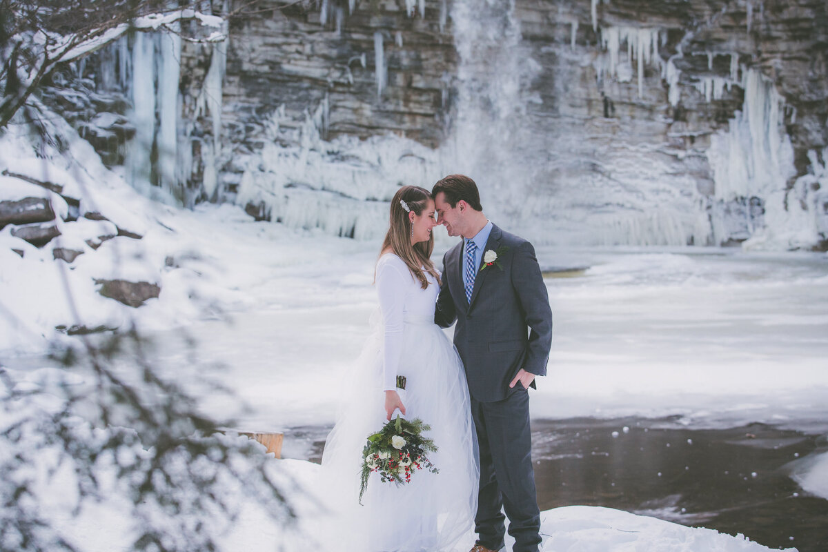 Couple touches foreheads with waterfall view in winter surrounded by snow.
