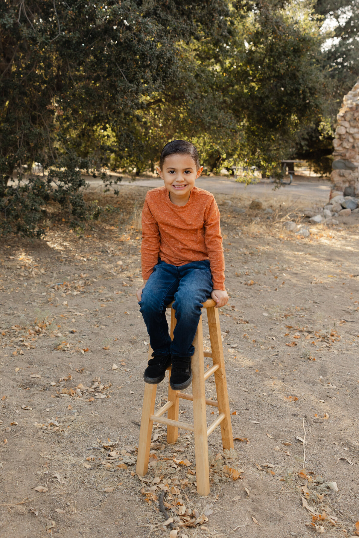 Young boy standing outdoors in orange sweater and jeans, smiling at the camera. Photographed by Yucaipa family photographer Kaitlyn Dawn Photography.