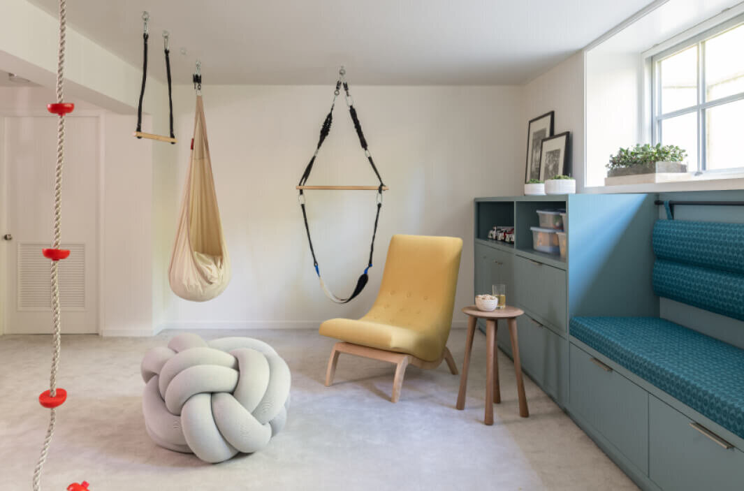 Boston area decorators design a kids' playroom with green built-ins, yellow lounge chairs, and a collection of hanging swings for a fun and functional space.