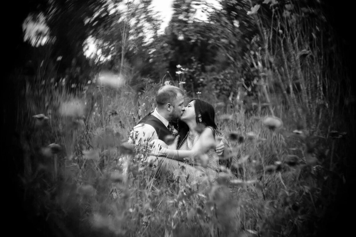 A soft-focused, monochrome image of a couple seated amidst tall grass