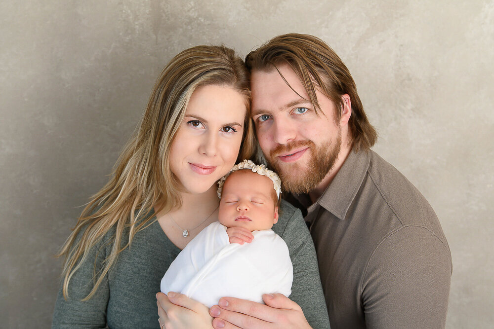Parents holding their newborn baby girl wrapped in white for her baby photos in Hamilton, Ontario.