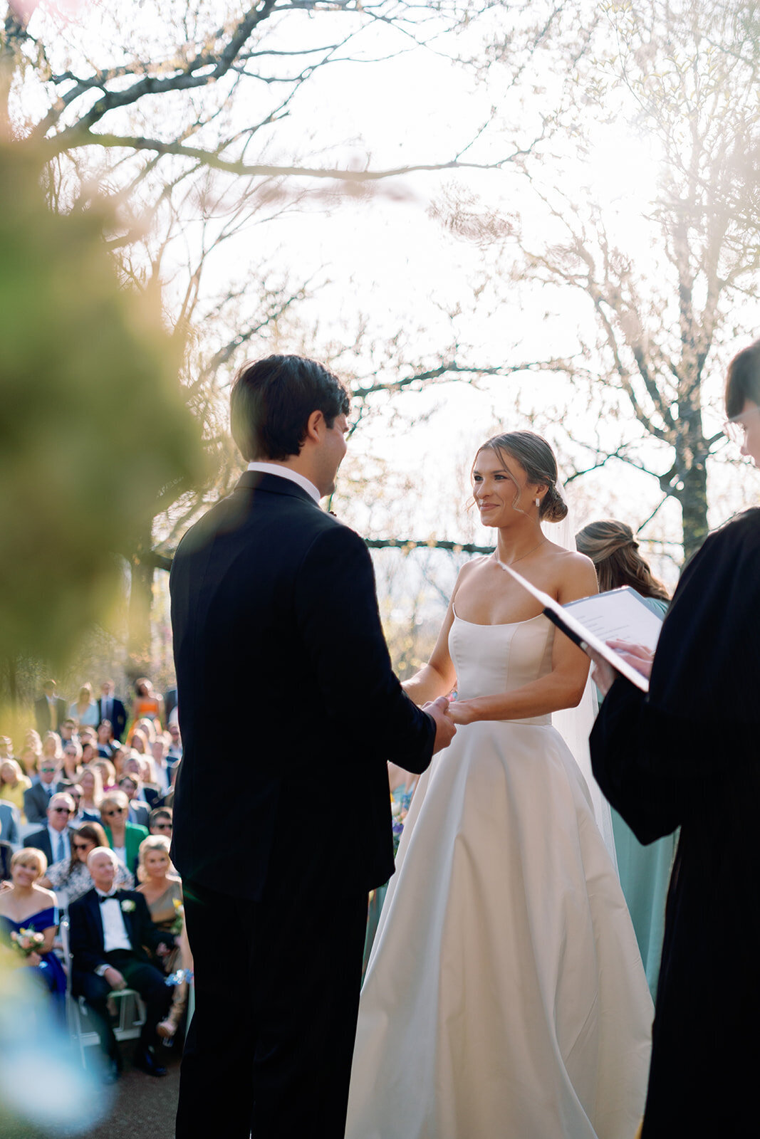 Bride and groom holding hands and looking at each other while exchanging vows during their outdoor wedding ceremony at Burritt on the Mountain in Huntsville, Alabama, photographed by Perry Hancock.