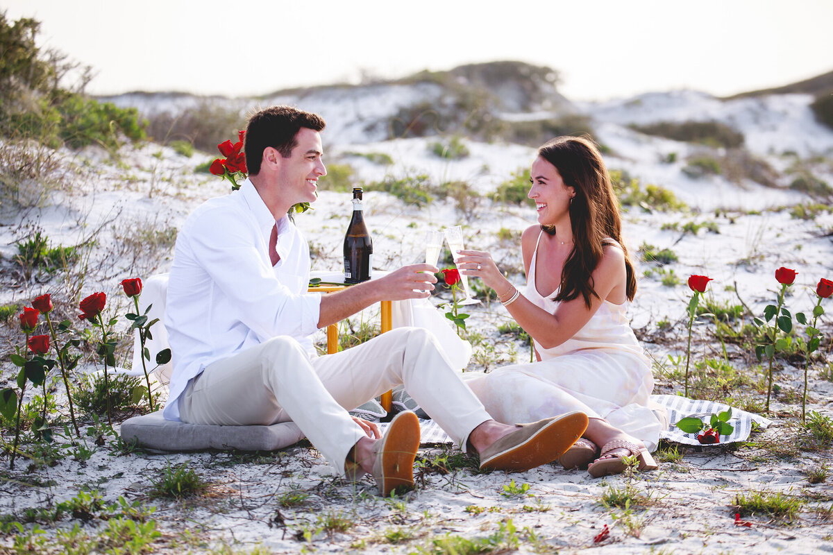 couple sitting on surprise proposal decor after she said yes and sipping champagne. 
