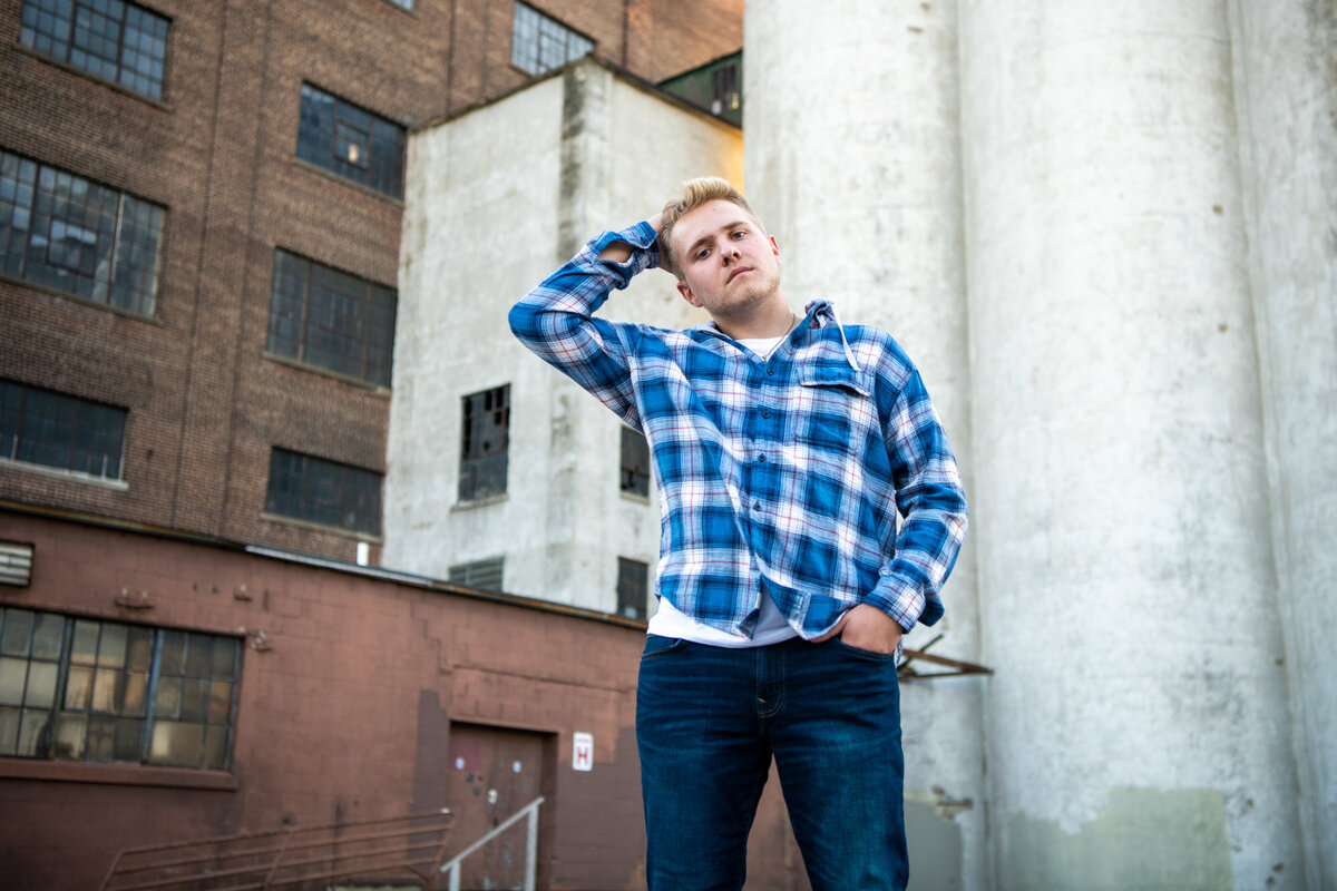 senior photo of boy in plaid shirt against warehouse