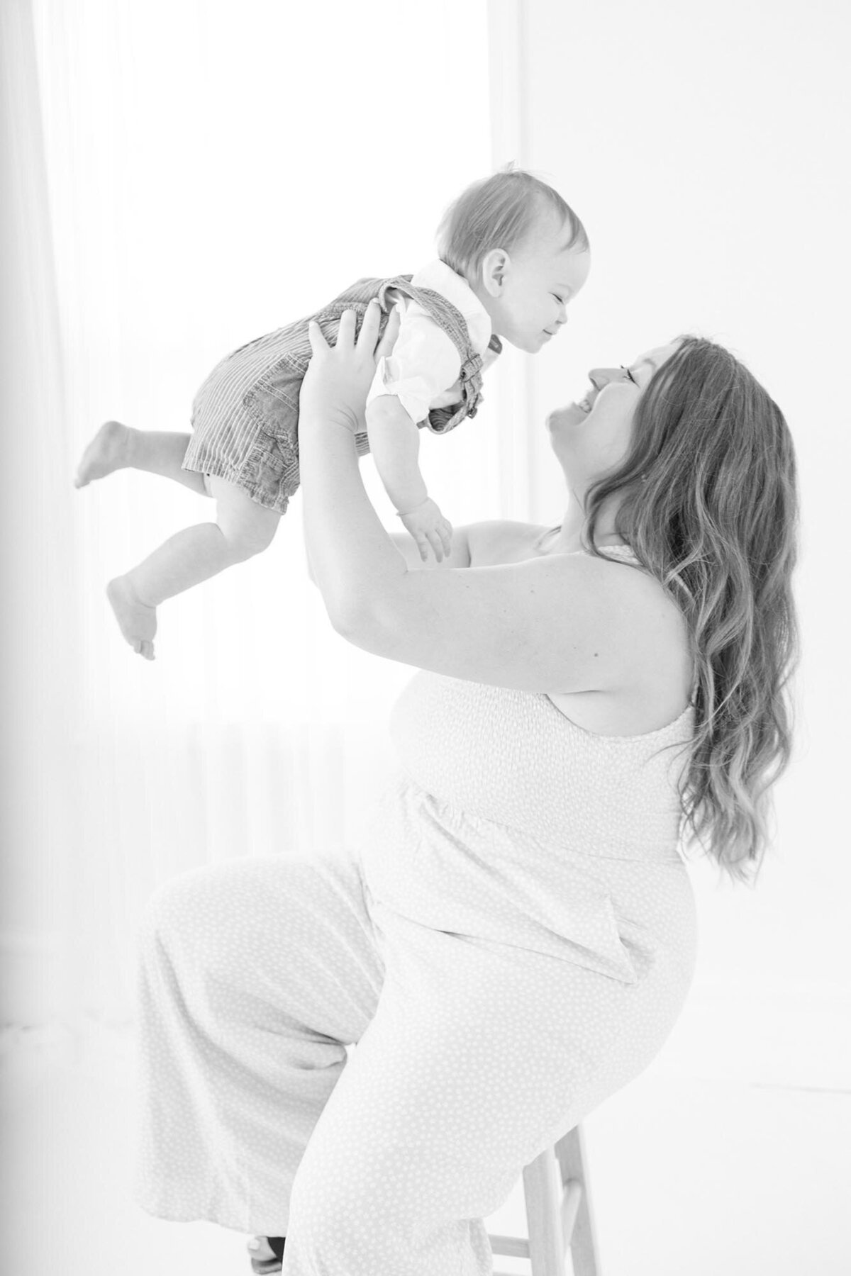 Black and White Family Photography of a Mother holding up her her one year old son in the air smiling at him in Virginia Beach
