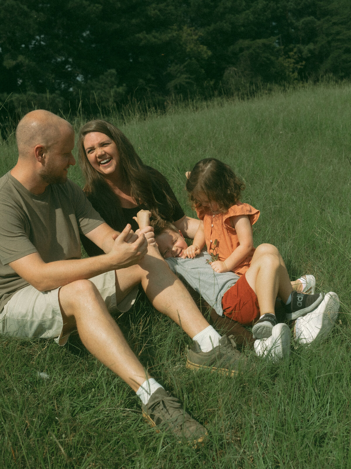 A family of four sitting in the grass at Noonday Creek Trail on a bright sunny day. 