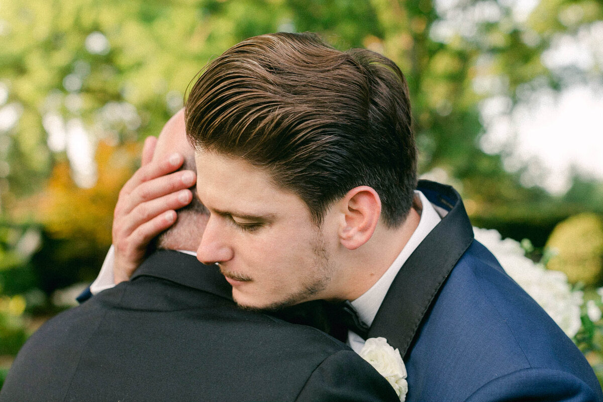 man in blue tuxedo hugging father in black suit