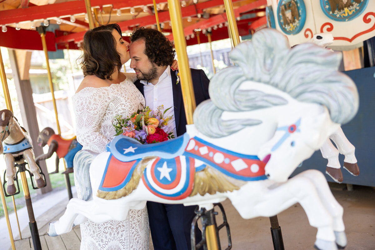 A bride kissing a groom's forehead as they are on a merry go round