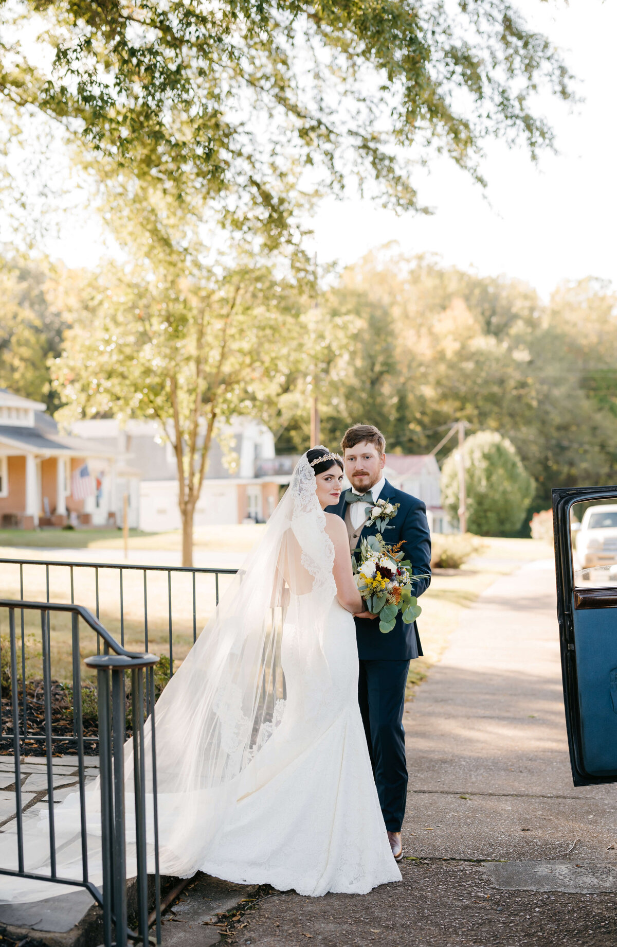 bride and groom on a side walk with their Richmond wedding chapel in the background as the couple embraces before getting into a vintage car that is parked next to them