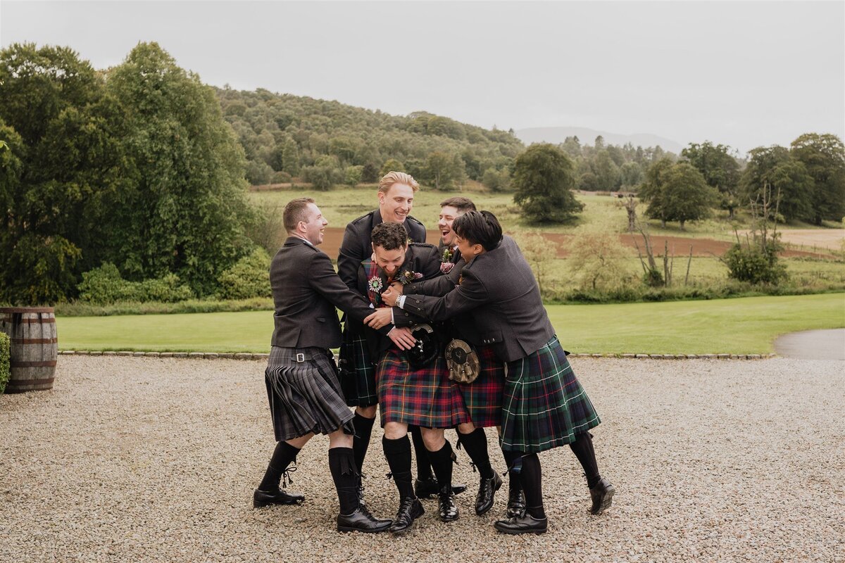 Four groomsmen bear hug a groom in the courtyard of Logie County House.