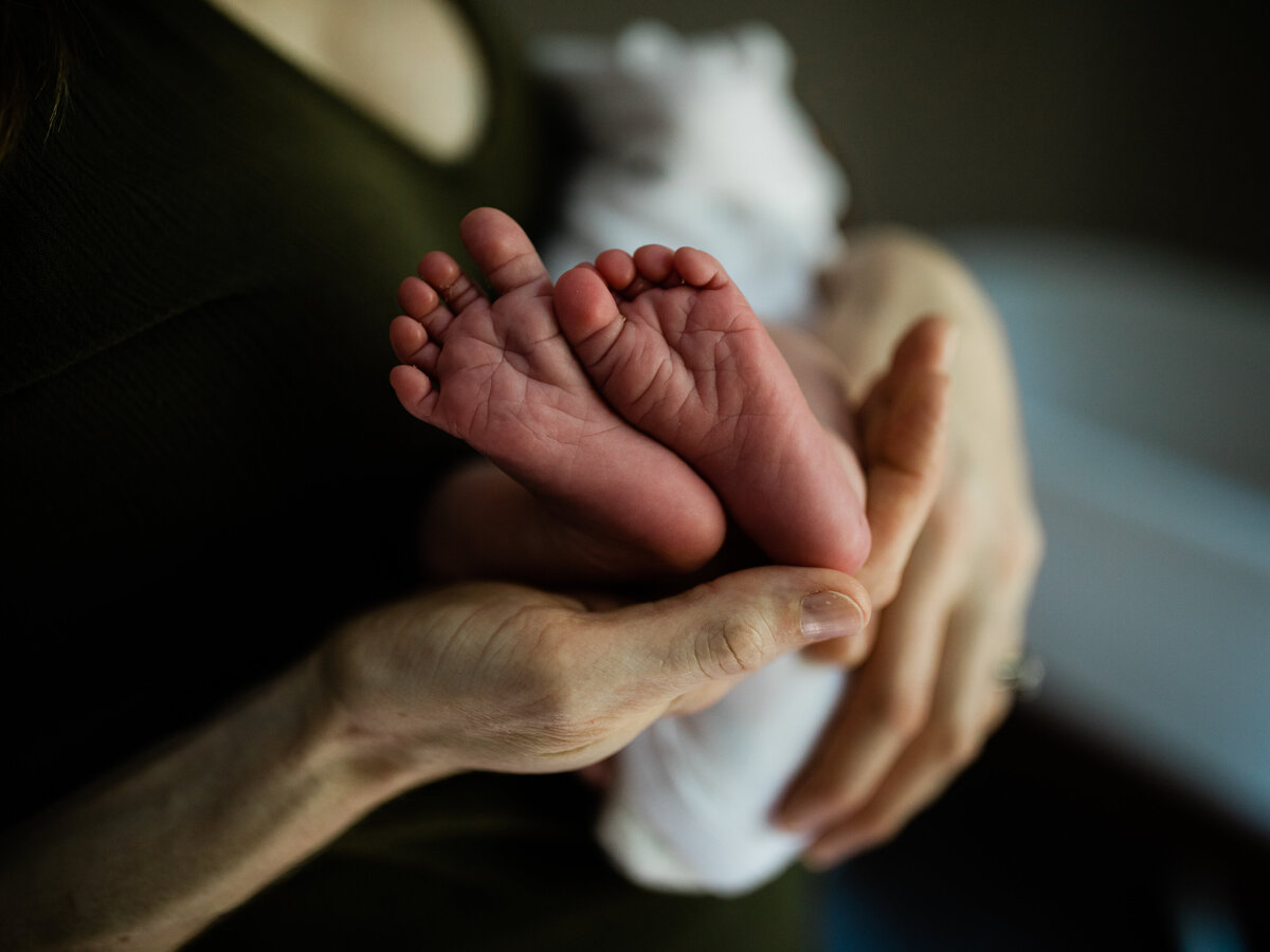 mom holding newborn baby boy showing feet
