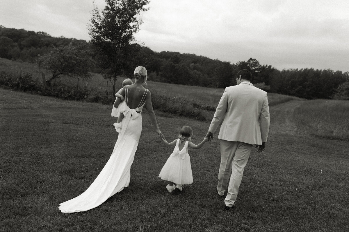 Bride and groom stroll hand-in-hand through a field with their flower girls.