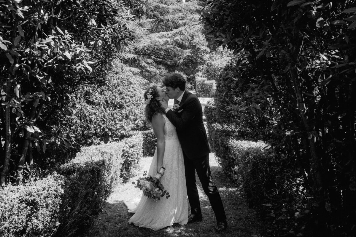 Black and white wedding photography of bride and groom kissing in a garden.