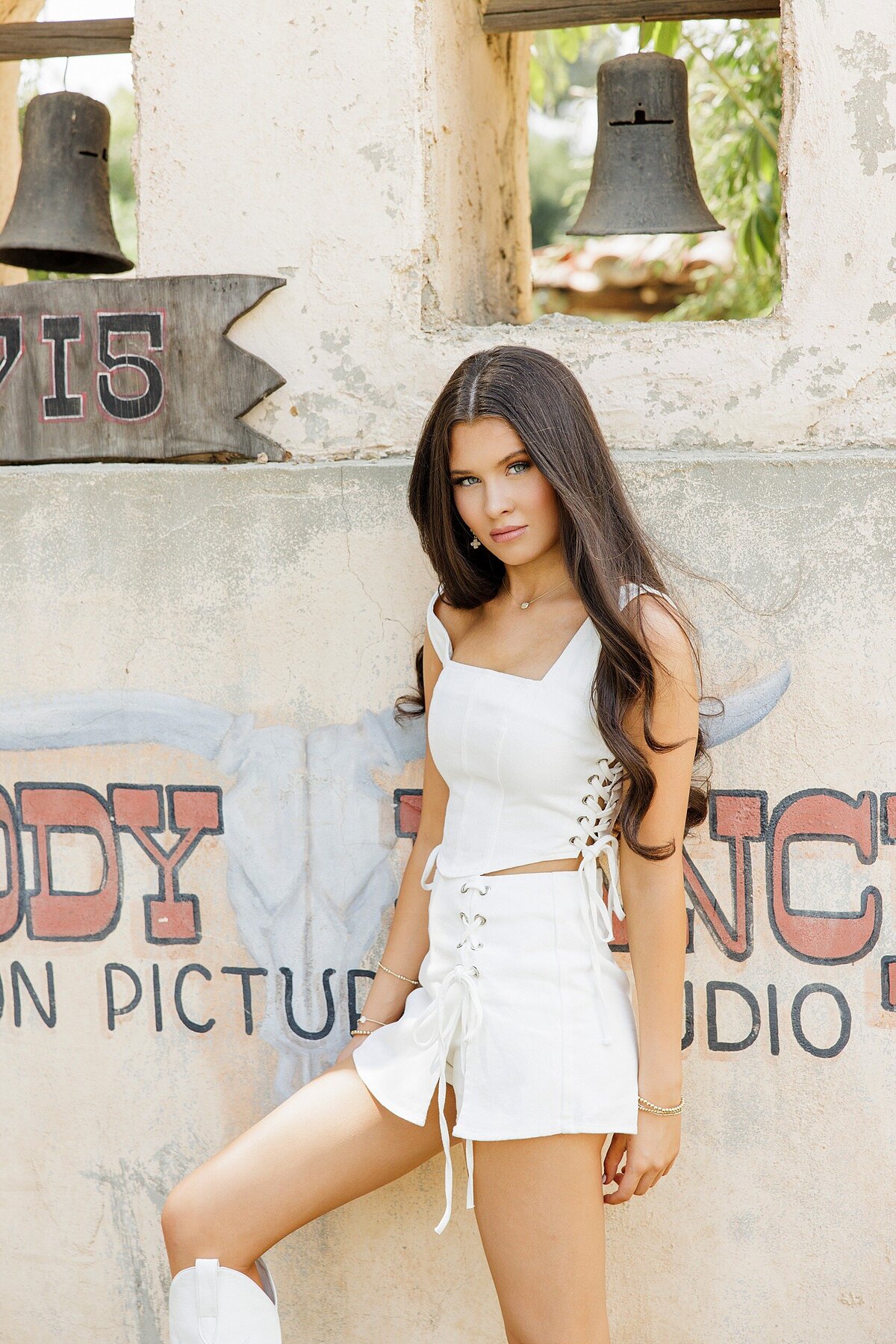 Editorial senior portrait in front of the iconic Melody Ranch Western movie set, wearing a white dress and boots.