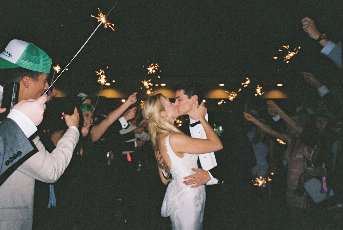 A captivating moment as the bride and groom share a kiss during their sparkler exit, surrounded by celebration and light, beautifully captured on film by Morgan Alysse, Louisiana film photographer.