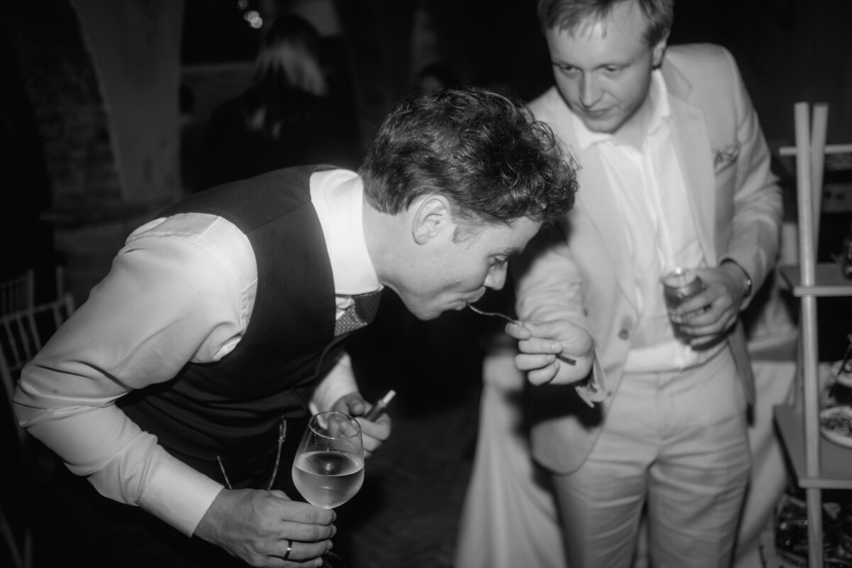 The groom eats cake during the wedding party with a guest.