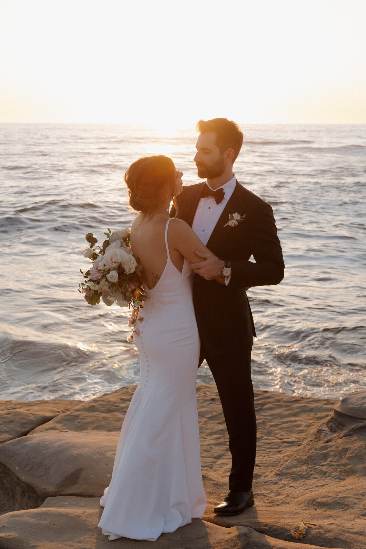 Romantic embrace of a couple at the La Jolla cliffs, overlooking the ocean, with cinematic golden hour wedding photography.