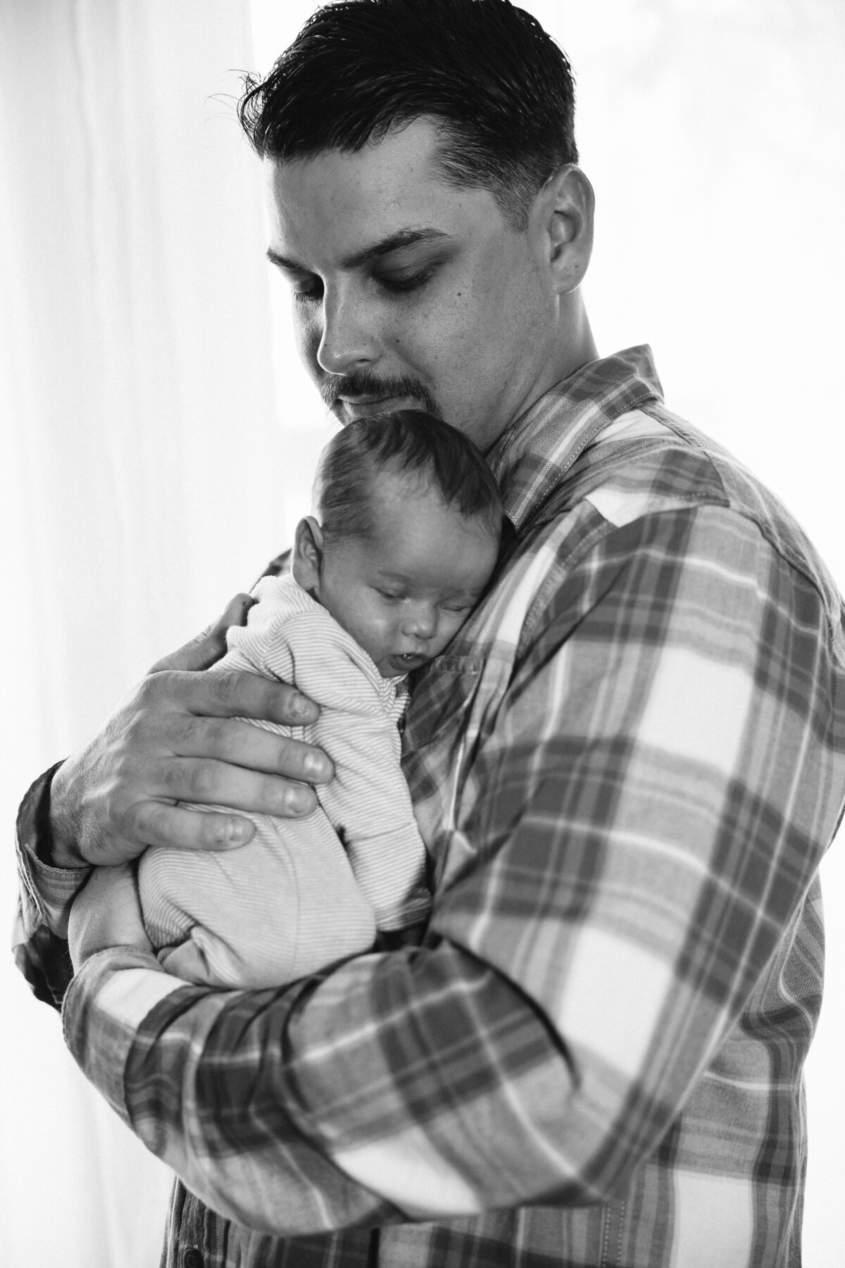 A newborn sleeps on dad's chest as he stands in a studio window
