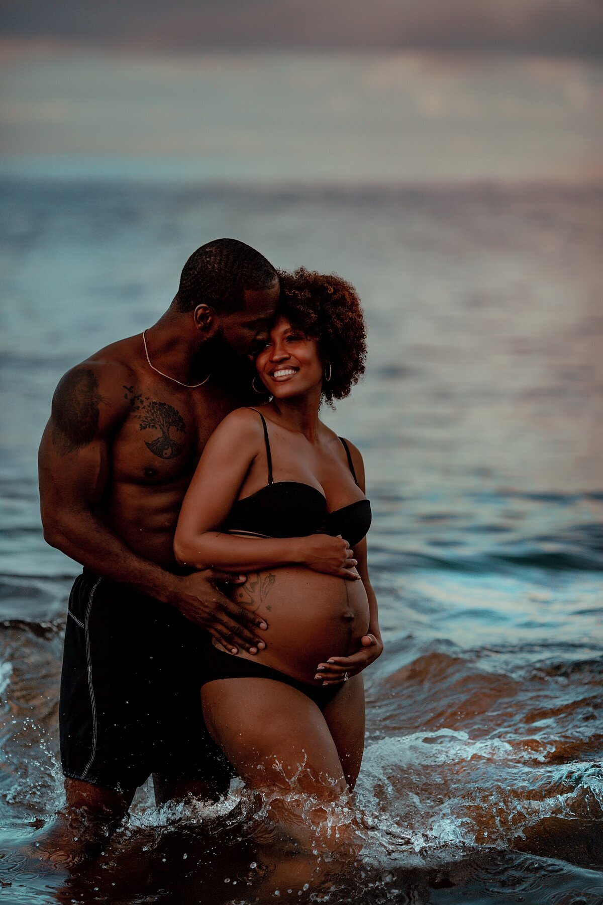 Couple embracing in the ocean for their Maternity portraits with Love + Water