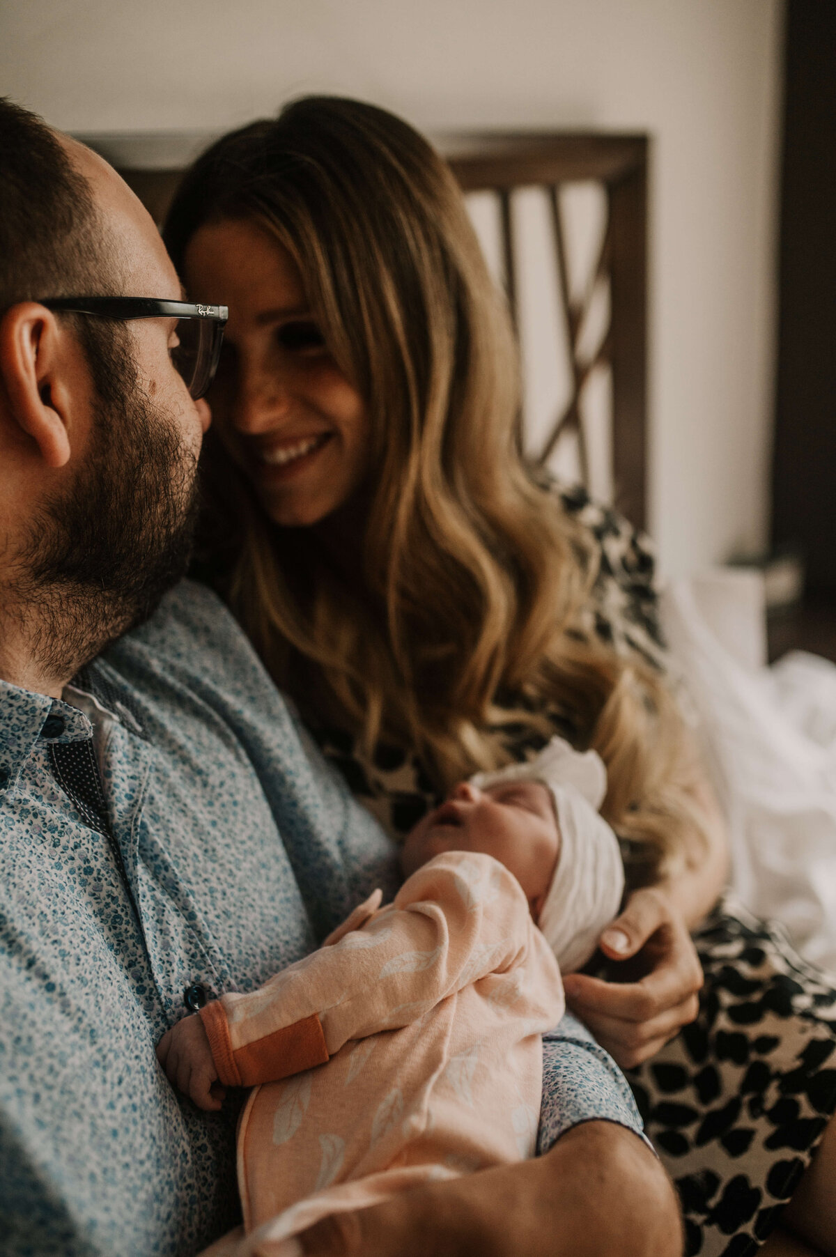 Newborn baby sleeps in fathers arms with mom watching