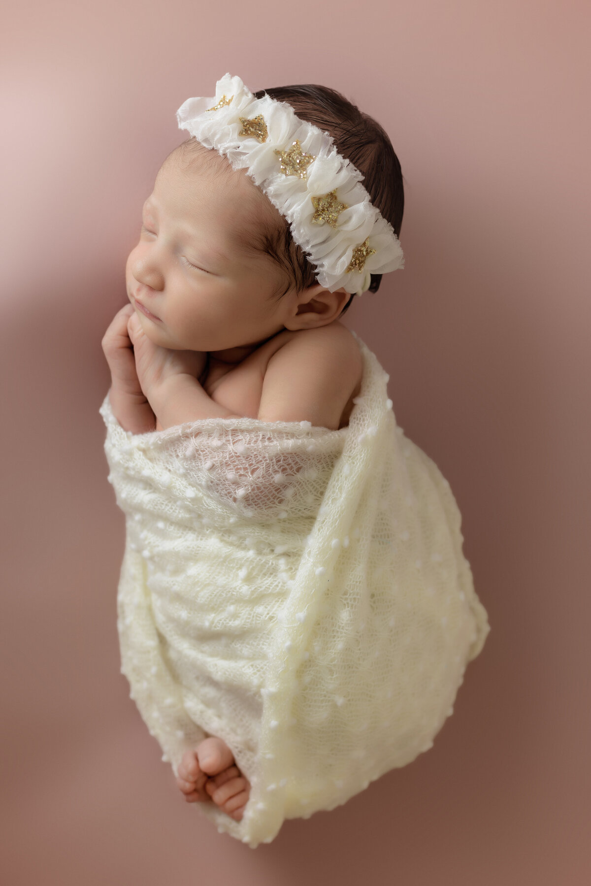 Newborn Photographer, a baby is swaddles in a thin ornate blanket with a matching headband