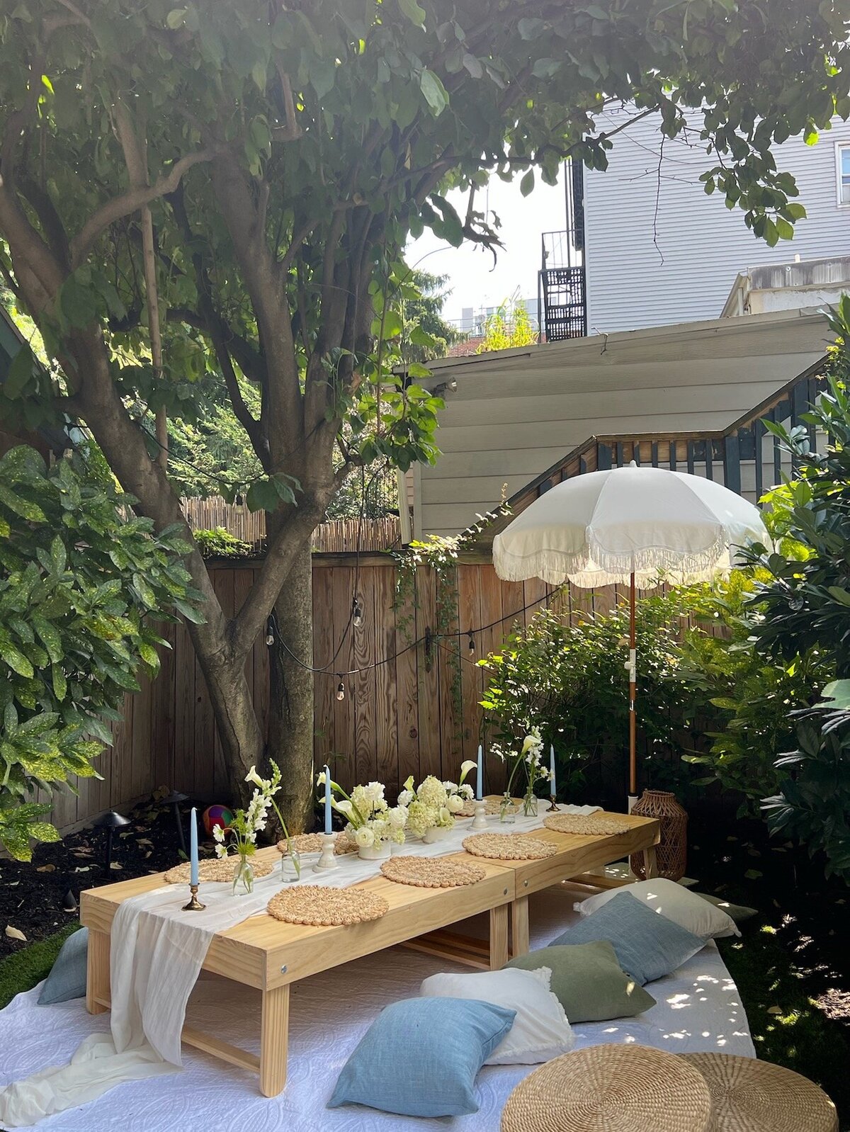 Intimate backyard picnic table with woven placemats, white florals, and a fringe umbrella, styled by Yours Truly, a wedding planner and designer in New Jersey.
