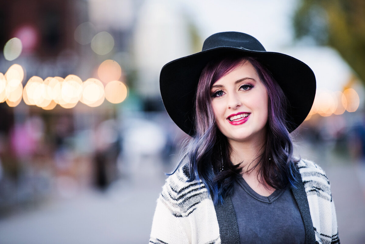 high school senior girl wearing black hat in urban street with streetlights