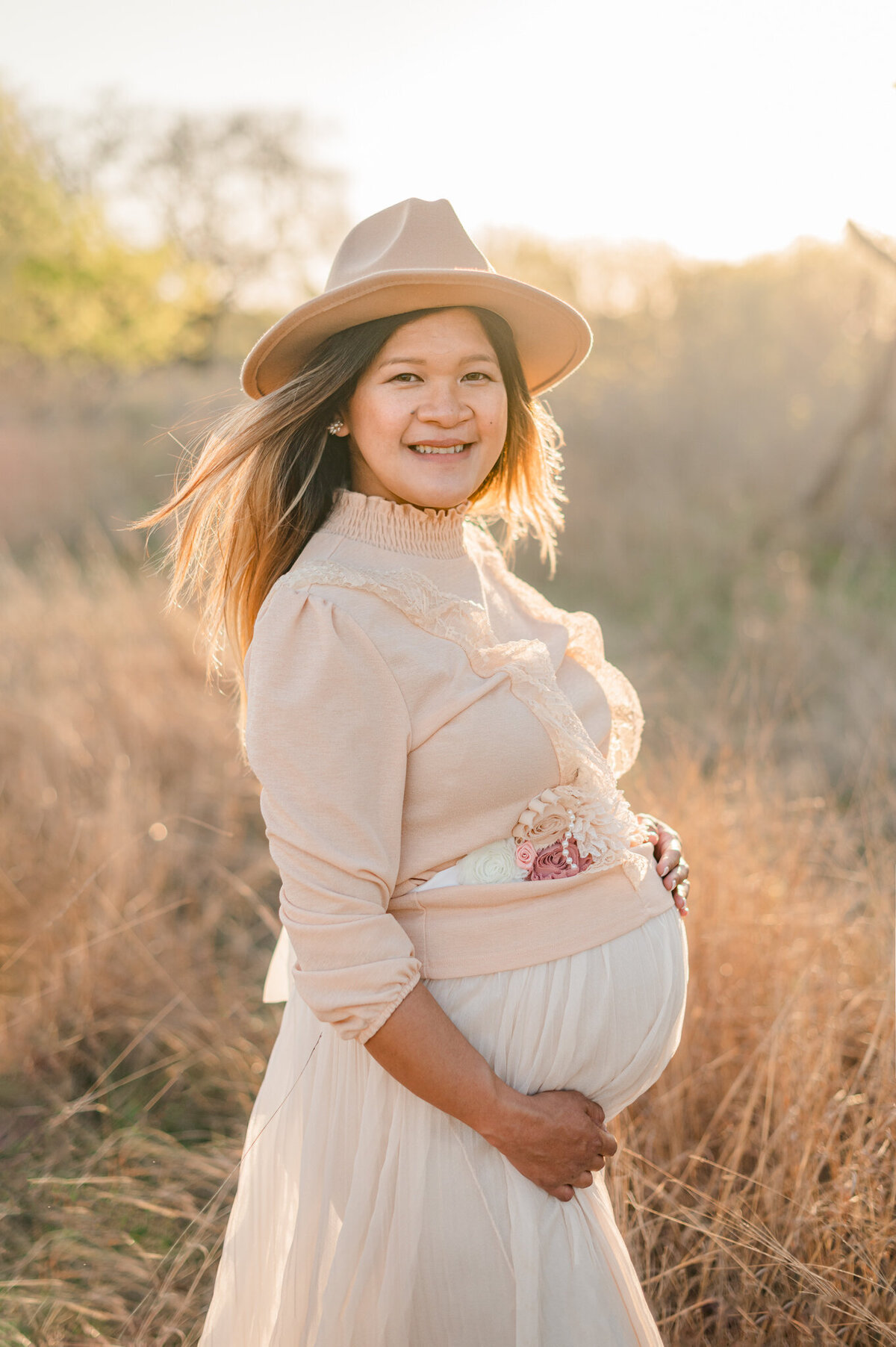 Woman holding her bump and smiling at the camera of San Antonio maternity photographer Cassey Golden.