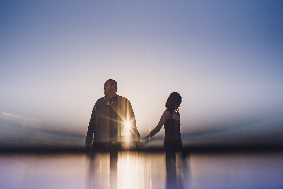 Couple holding hands at sunset with reflection at bottom of the frame