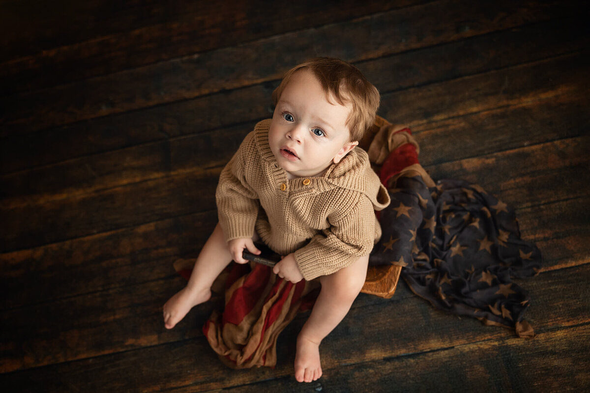 Baby boy sits in a wooden heart bowl donned with a flag pattern scarf.