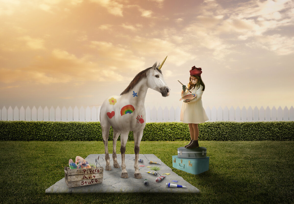 A magical image of a little girl standing on her suitcases painting doodles on a unicorn