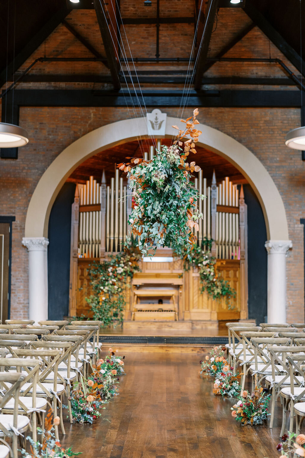 Lush and whimsical asymmetrical installation highlighting the organ was filled with greenery, autumnal foliage, and garden roses. Floral Design by Rosemary and Finch in Nashville, TN.