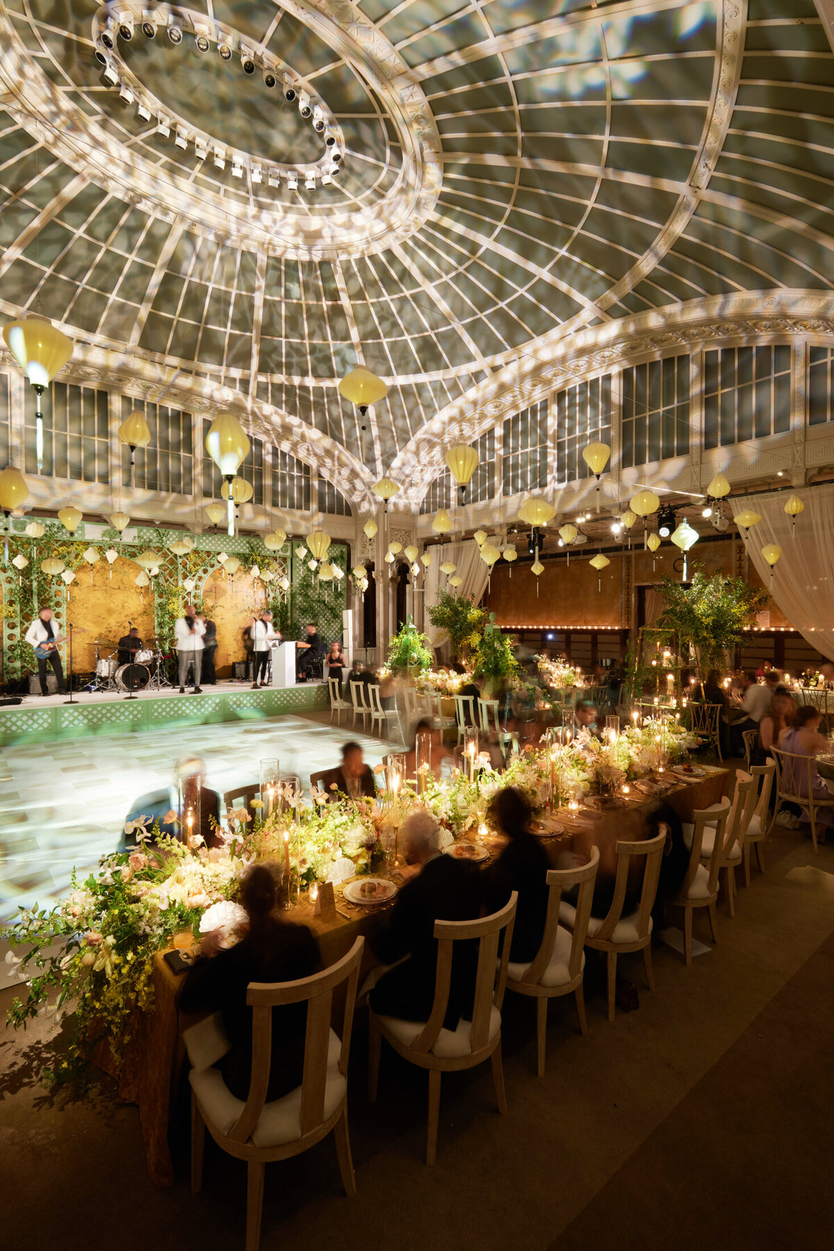 The luxurious wedding reception in a grand, glass-domed venue at the iconic New York Public Library in New York City was beautifully captured by photographer Shawn Connell and videographers Aaron Navak Films. Long dining tables at the reception were elegantly adorned with floral arrangements and candles, creating a romantic and sophisticated atmosphere. As guests enjoyed the elegant setting, a well-lit stage and a band were set up in the background, adding to the ambiance and entertainment of the evening.