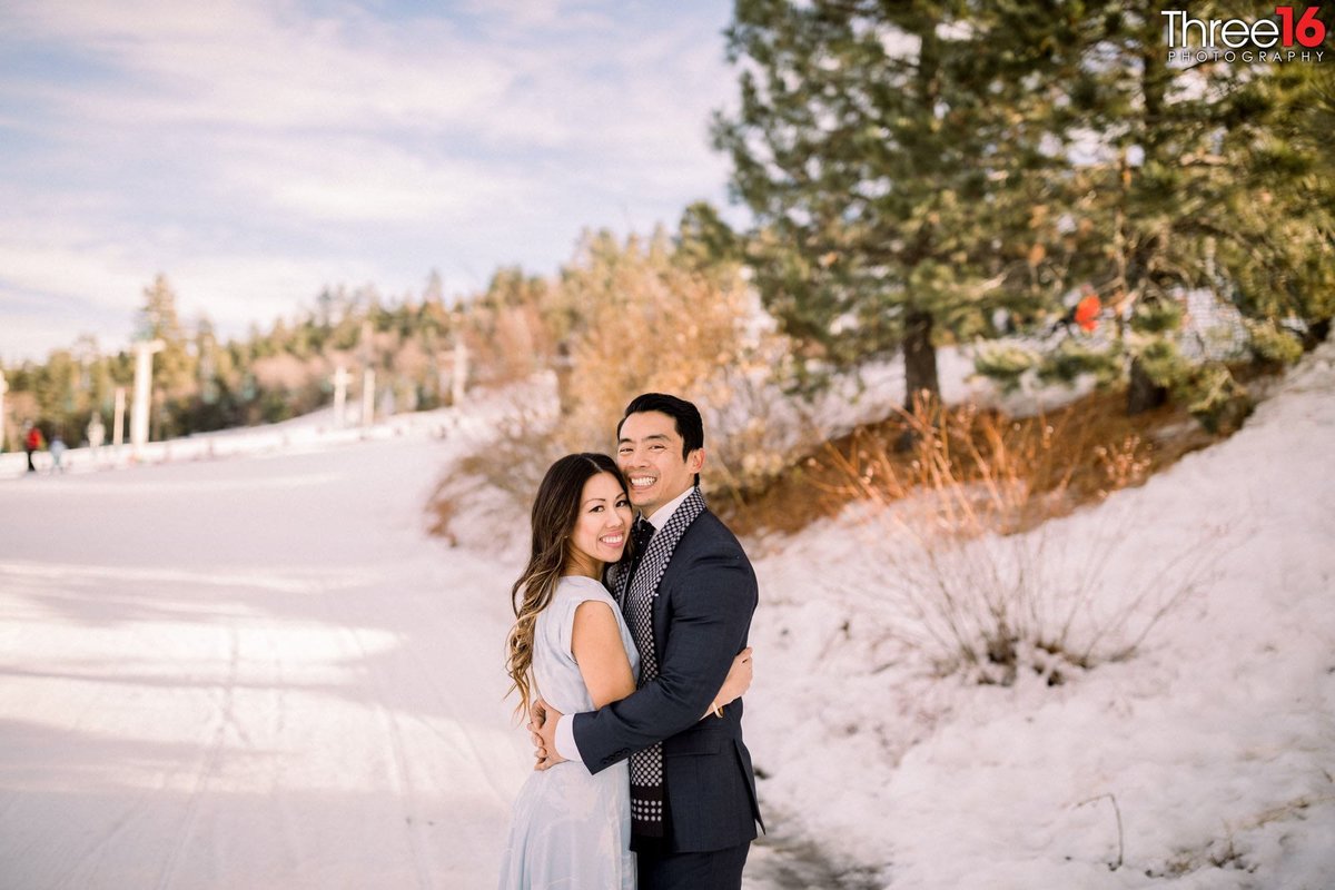 Engaged couple fully embrace one another on the snowy ground of Snow Summit